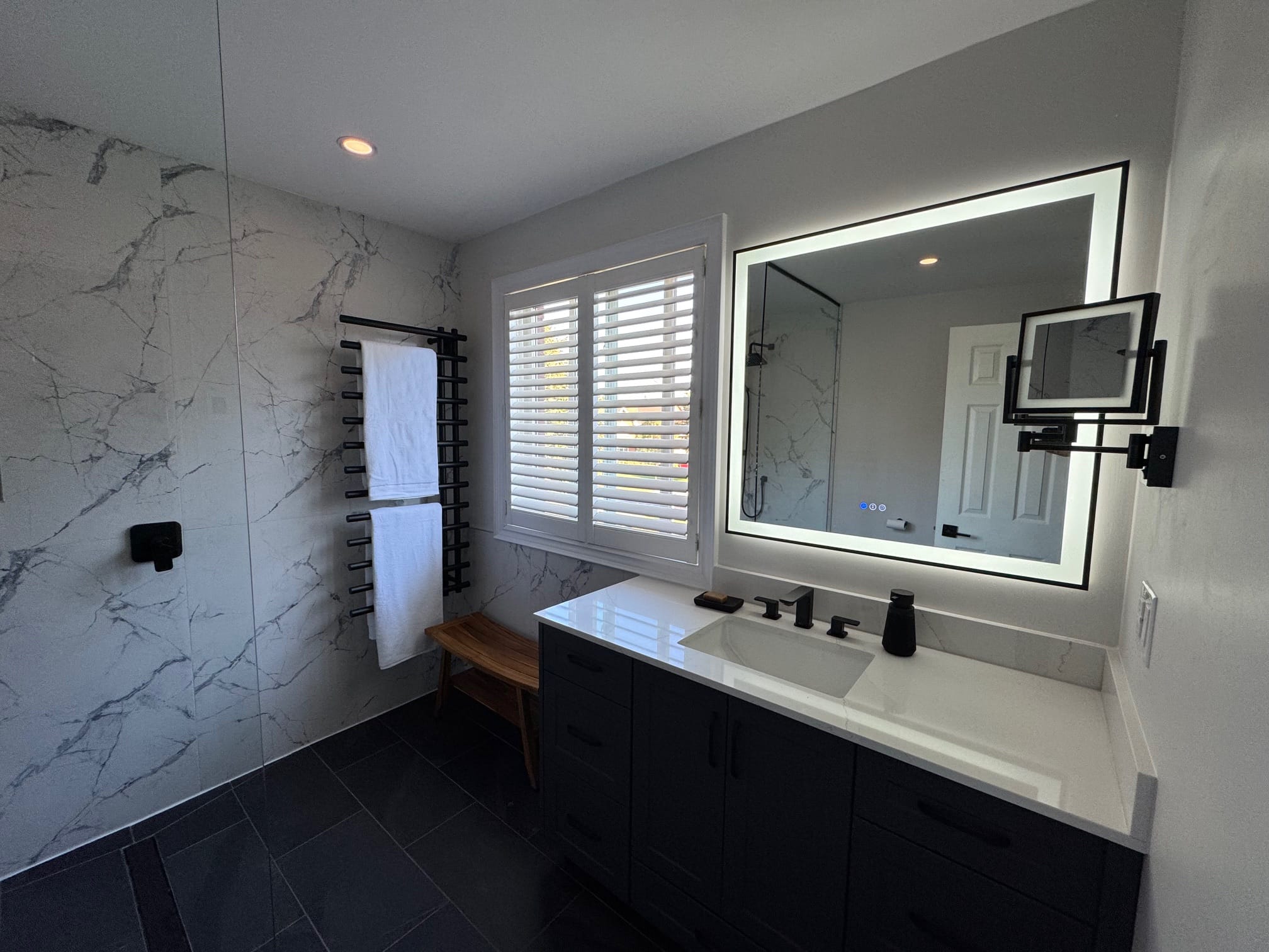 Renovated bathroom with a long vanity, lit mirror and walk-in shower